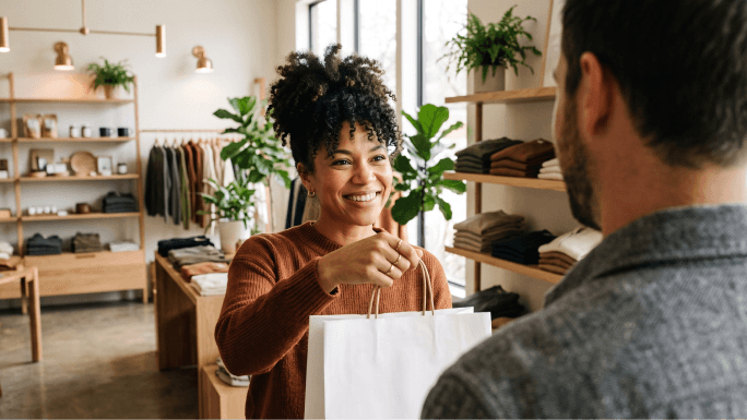 Inhaber eines Kleinunternehmens überreicht einer Kundin beim Bezahlen eine Boutique-Einkaufstasche.