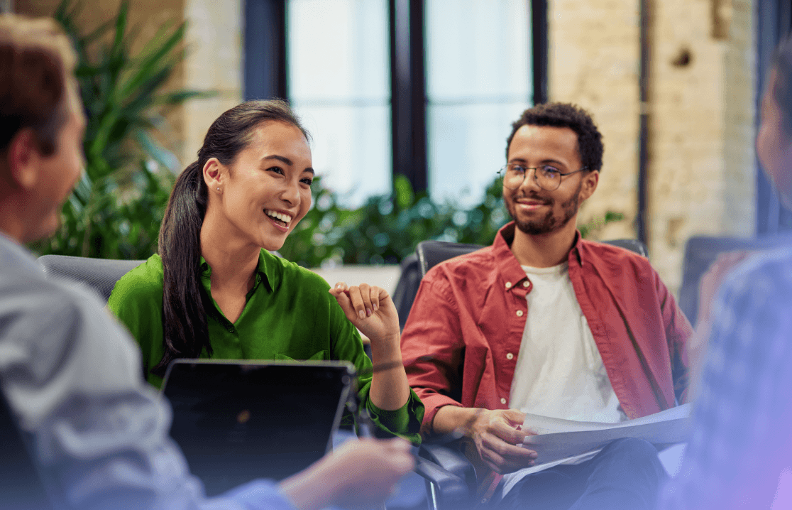 Verschiedene Kollegen lächeln und diskutieren gemeinsam Dokumente bei einem modernen Büro-Meeting.